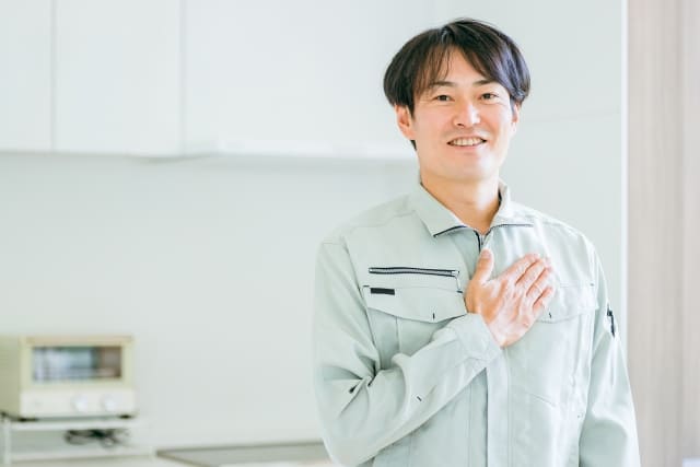 電気工事士がキッチンを背景に胸に手を当てこちらを見ている画像